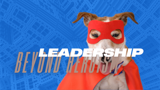 Color image of a dog wearing a red superhero mask and cape against a blue background, with the words "LEADERSHIP BEYOND HEROISM" overlaid.